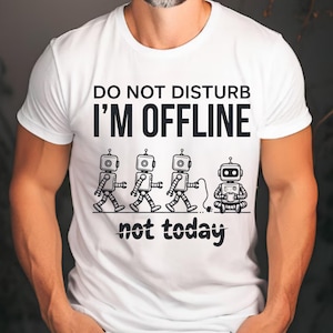 May include: White t-shirt with the text "DO NOT DISTURB I'M OFFLINE not today." The graphic features four cartoon robots. Three robots are walking, and one is sitting cross-legged, holding a cup.