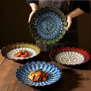 Op de afbeelding: Een verzameling decoratieve keramische borden met geschulpte randen en ingewikkelde bloempatronen. De borden hebben verschillende kleuren, waaronder blauw, groen, rood en bruin. Sommige borden bevatten voedsel.