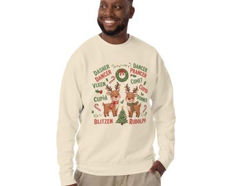 May include: Cream-colored sweatshirt featuring a festive Christmas design. The graphic includes two reindeer, a Christmas tree, candy canes, and the names of Santa's reindeer. The text includes "Dasher, Dancer, Vixen, Cupid, Blitzen, Rudolph".