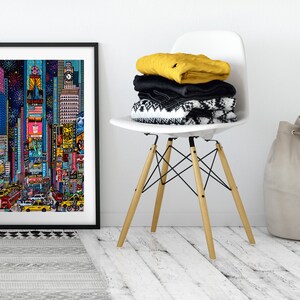 Puede incluir: Una impresi&oacute;n enmarcada de una ilustraci&oacute;n colorida de Times Square en la ciudad de Nueva York por la noche. La ilustraci&oacute;n presenta edificios, vallas publicitarias y personas caminando por la calle. La impresi&oacute;n est&aacute; colgada en una pared blanca sobre una alfombra de patr&oacute;n gris y negro.