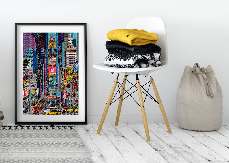 Puede incluir: Una impresi&oacute;n enmarcada de una ilustraci&oacute;n colorida de Times Square en la ciudad de Nueva York por la noche. La ilustraci&oacute;n presenta edificios, vallas publicitarias y personas caminando por la calle. La impresi&oacute;n est&aacute; colgada en una pared blanca sobre una alfombra de patr&oacute;n gris y negro.