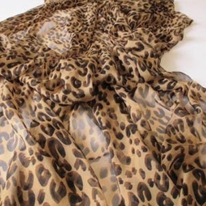 May include: A leopard print fabric in shades of tan and brown. The material is lightweight and appears to be draped, with visible folds and a sheer quality. The pattern features dark brown spots.