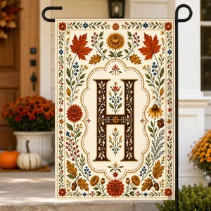 May include: A rectangular garden flag featuring a large, dark brown letter H centered within an ornate frame. The design includes autumn-themed illustrations of orange maple leaves, yellow chrysanthemums, red berries, and acorns on a cream background.