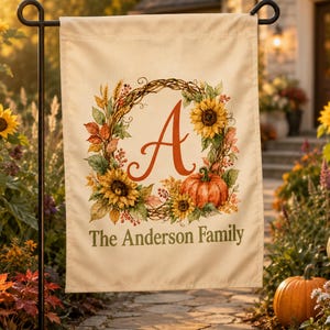 May include: A rectangular cream-colored garden flag hanging on a black metal stand. The flag features a central wreath of sunflowers, autumn leaves, and a pumpkin surrounding a large orange letter A. The text The Anderson Family is printed below.