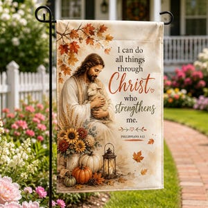 May include: A rectangular garden flag featuring an illustration of a person with long hair holding a small lamb. The text reads, I can do all things through Christ who strengthens me. Philippians 4:13. Includes autumn leaves, sunflowers, pumpkins, and a lantern.