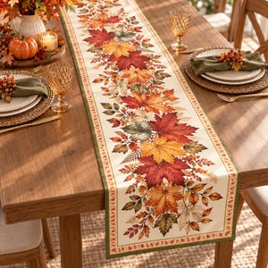 May include: A rectangular table runner featuring a central print of vibrant autumn maple leaves in shades of red, orange, yellow, and green on a cream background, bordered by a thin green trim and a repeating pattern of small leaves.