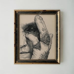 May include: A framed black and white ink illustration on a beige background depicting a hand covering half of a face. The hand features detailed line work, a large ornate ring on the ring finger, a smaller ring on the index finger, and a tattoo.