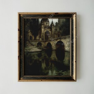 May include: A framed wall art print depicting a dark, moody stone building with arched bridges over a reflective body of water. The scene features stone steps leading to the water and a tall, domed structure. The frame is dark wood with gold trim.