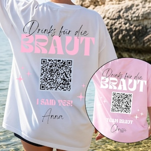 Könnte beinhalten: Weißes T-Shirt mit dem Text "Drinks für die BRAUT" in schwarzer Schrift und rosa Blockbuchstaben. Darunter ein QR-Code, der Text "I SAID YES!" und der Name "Anna". Ein kleineres rosa T-Shirt zeigt den Text "TEAM BRAUT" und den Namen "Chrissi".