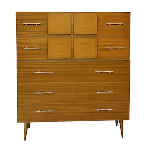 May include: A mid-century modern dresser with a warm wood grain finish. It features multiple drawers with silver-toned handles and a unique square design on the top section. The dresser stands on tapered legs.