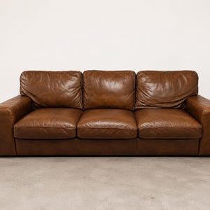 May include: A three-seat sofa upholstered in brown leather. The piece features three distinct back cushions and three seat cushions, all with a smooth, slightly worn texture. The frame includes wide, square armrests on both the left and right sides.