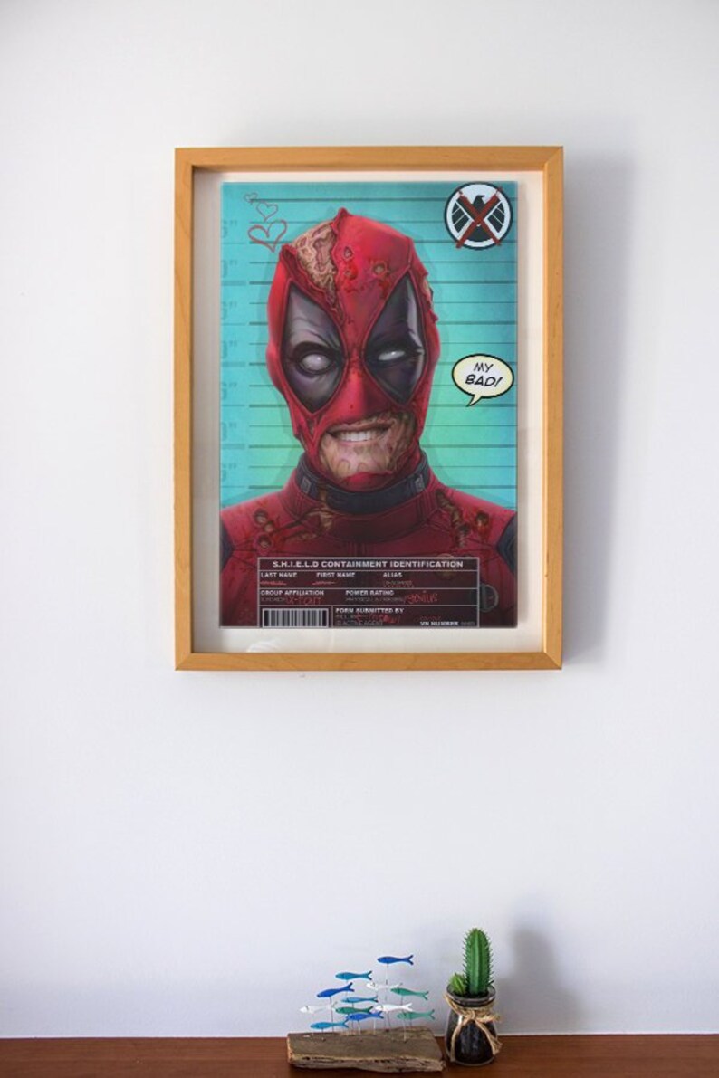 May include: A framed print of a comic book character, Deadpool, wearing a red and black costume, a mask, and a speech bubble that says "My Bad!" The print is in a wooden frame and has a blue and green background with a S.H.I.E.L.D. logo.