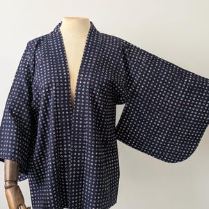 Può includere: Una giacca in stile kimono blu navy scuro caratterizzata da un motivo all-over di piccoli punti circolari bianchi e rosa chiaro. Il capo presenta maniche larghe e ampie, un'apertura frontale dritta e uno scollo senza colletto.
