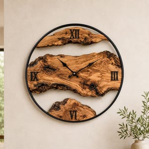 May include: A round wall clock featuring a thin black metal frame and three distinct pieces of natural light brown wood with visible grain and knots. The clock face displays black Roman numerals at the XII, III, VI, and IX positions.