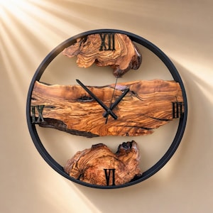 May include: A circular wall clock featuring a black metal frame and three distinct pieces of natural wood with visible grain patterns. The clock face includes black Roman numerals at the twelve, three, six, and nine o'clock positions and black hands.