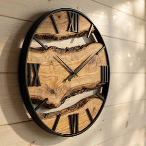 May include: A circular wall clock featuring a natural wood face with black Roman numerals. The clock face has an organic shape, set within a dark, circular metal frame. The clock hands are black.