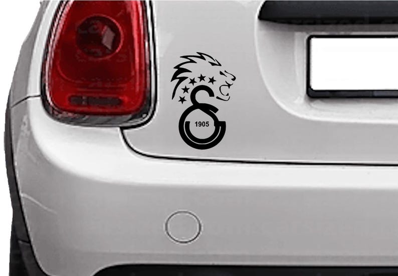 Puede incluir: Calcoman&iacute;a negra para coche con la cabeza de un le&oacute;n, estrellas y las letras "GS" con el n&uacute;mero "1905" en un coche blanco. El le&oacute;n tiene una melena detallada y mira hacia la derecha.