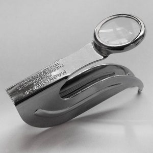 May include: A silver magnifying glass with a clip on the back. The magnifying glass is attached to a silver metal handle. The handle has the text "MAGNI-TWIR 2X PRECISE PRODUCTS 5100000015 TEMPLE CITY, CALIF."