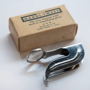 May include: A silver magnifying tweezer with a built-in magnifying glass. The tweezer is in its original packaging, which is a brown cardboard box with the text "NO. 313 MAGNI-TWEZE The new tweezer with built-in magnifying glass BAUER-LEE & CO. SIERRA MADRE 1, CALIF." printed on it.