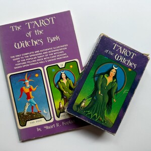 May include: Two vintage tarot card decks and a book titled "The Tarot of the Witches Book." The book is purple with white text and illustrations of tarot cards. The deck on the right is purple with a woman in green. The other deck shows "The Fool" card.