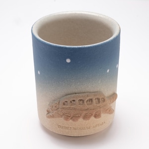 May include: Ceramic tumbler with a blue and beige gradient. The design features a relief of a bus with passengers, and the text "GHIBLI MUSEUM MITAKA" is printed at the bottom. White dots are scattered across the blue section.