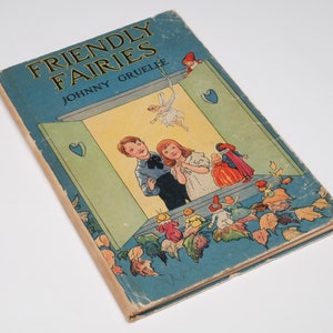 May include: A vintage children's book titled "Friendly Fairies" by Johnny Gruelle. The cover features a blue background with a window scene, a fairy flying, and children looking out the window. There are also several small fairies and leaves on the cover.