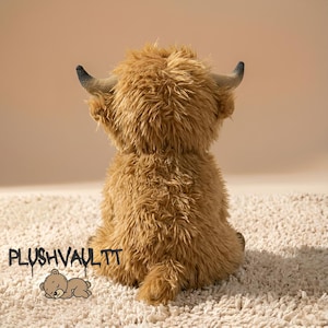 Fluffy brown Highland cow plushie sitting on a soft rug. Cute Scottish cow stuffed animal with long shaggy hair and horns.