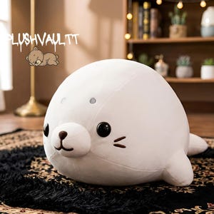 Puede incluir: Un peluche blanco con forma de foca, con grandes ojos negros, una pequeña nariz marrón y bigotes. El juguete está sobre una alfombra negra estampada. El texto "PLUSHVAULTT" es visible en la esquina superior izquierda.