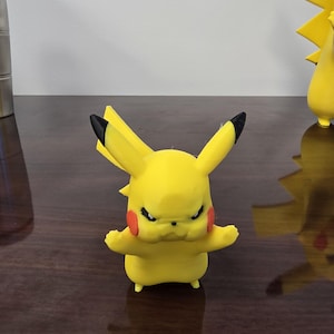 May include: A yellow Pikachu figurine with black-tipped ears and red cheeks. The figure has an angry expression and outstretched arms. A second Pikachu figure is visible in the background.