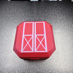 Op de afbeelding: Een rode, achthoekige, 3D-geprinte opbergdoos met een wit grafisch ontwerp op het deksel. Het ontwerp bestaat uit twee verticale rechthoekige panelen, elk met een kleinere rechthoek met een X-vorm erin, lijkend op een staldeurmotief.