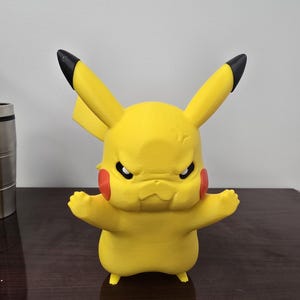 May include: A yellow Pikachu figurine with black-tipped ears, red cheek patches, and an angry expression. The figure has outstretched arms and small feet, and is set against a neutral background.