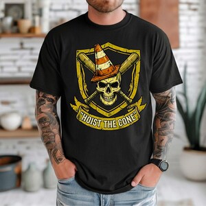 May include: Black t-shirt featuring a skull wearing a traffic cone, crossed baseball bats, and the text "HOIST THE CONE" in a banner. The design is in yellow and orange tones.
