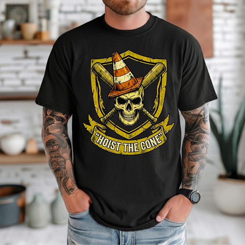 May include: Black t-shirt featuring a skull wearing a traffic cone, crossed baseball bats, and the text "HOIST THE CONE" in a banner. The design is in yellow and orange tones.