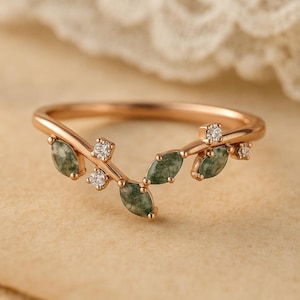 Può includere: Anello in oro rosa con design a foglie. L'anello presenta pietre preziose verdi taglio marquise e piccoli diamanti scintillanti. L'anello è posto su uno sfondo neutro.