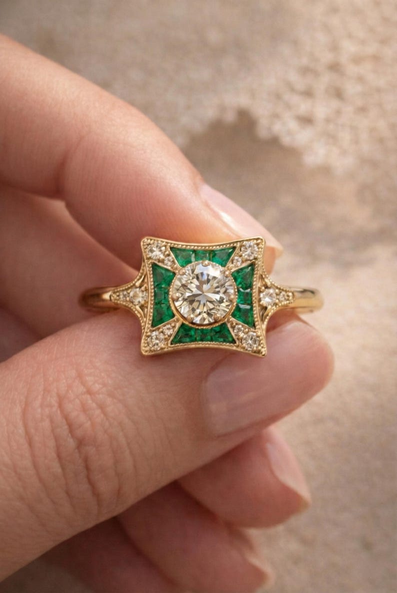 May include: A gold ring featuring a central round diamond, surrounded by emerald-colored stones and smaller diamonds. The ring has an Art Deco design with a square-shaped setting and a delicate band.