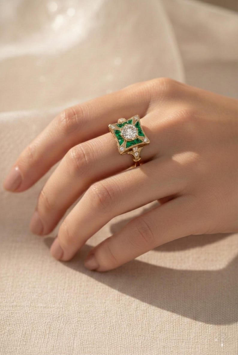 May include: A gold ring with a square emerald and diamond design. The ring features a central round diamond surrounded by green emeralds and smaller diamonds. The ring is on a person's finger.
