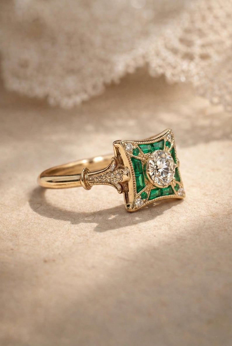 May include: A gold ring with a square emerald and diamond design. The center features a round diamond, surrounded by emeralds and smaller diamonds. The ring has a detailed band and a vintage aesthetic.