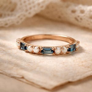 Könnte beinhalten: Roségoldener Ring mit abwechselnd blauen und weißen Edelsteinen. Der Ring hat ein warmes Roségold, und die Edelsteine sind in einem sich wiederholenden Muster angeordnet. Die blauen Steine sind rechteckig, die weißen Steine sind rund.