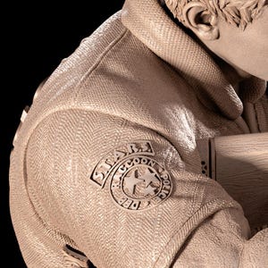 May include: A sculpture of a person wearing a jacket with a "STARS Raccoon Police DEP" patch. The jacket has a textured pattern and a high collar. The sculpture is in a neutral colour.