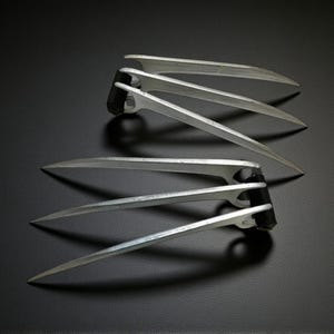 May include: A pair of silver metal claws, each with three sharp blades, resting on a dark surface. The claws are designed with a curved shape and a black base. The logo "PATNULL 3D STL" is in the upper left corner.