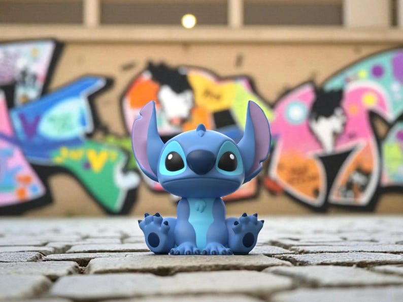 K&ouml;nnte beinhalten: Eine blaue Stitch-Figur mit gro&szlig;en Ohren und dunklen Augen sitzt auf einer Ziegeloberfl&auml;che. Die Figur befindet sich in sitzender Position, H&auml;nde und F&uuml;&szlig;e sind sichtbar. Der Hintergrund zeigt farbenfrohe Graffiti-Kunst.