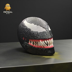 May include: A black and white Venom-themed 3D-printed object with a textured surface. The object features a wide, toothy grin with red gums and sharp white teeth. The top has a white section with small holes. The logo "PATNULL 3D STL" is visible.
