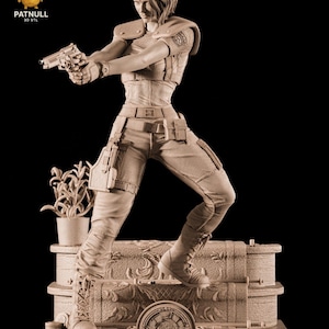 May include: A sepia-toned figurine of a woman in combat gear, holding a handgun. The figure is dynamically posed, with the text "Resident Evil" at the base. A small potted plant is also present in the scene.