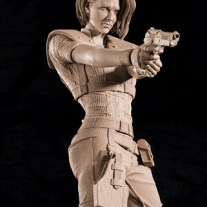 May include: A detailed sculpture of a person holding a handgun, dressed in tactical clothing. The figure has short hair and a determined expression. The outfit includes a ribbed top, tactical trousers, and a holster. The sculpture is in a neutral colour against a dark background.