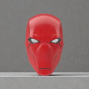 Może przedstawiać: Czerwona maska Red Hood z białymi soczewkami oczu i czarnymi konturami. Maska ma teksturowaną powierzchnię i określony kształt, z wyraźnym nosem i subtelnym otworem ust. Temat superbohatera.