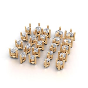May include: A collection of gold-toned jewelry settings arranged in rows, each featuring a clear, faceted gemstone held by four vertical prongs. The settings vary in shape, including round and pear-cut stones, all displayed on a plain white background.