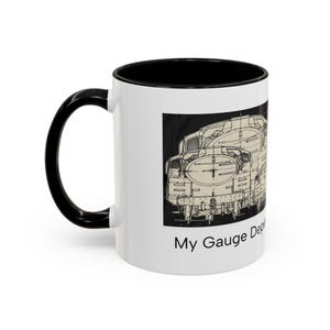 May include: A white ceramic mug with a black interior and handle, featuring a black and white technical line drawing of a steam locomotive on the side. Below the illustration, the text reads My Gauge Depends on You in black font.