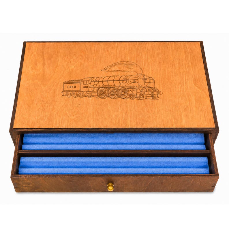 Op de afbeelding: Houten kist met een treingravure op het deksel. De kist is open en toont een blauw interieur met twee compartimenten. Hij heeft een goudkleurige knop aan de voorkant.