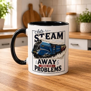 Puede incluir: Una taza de cer&aacute;mica blanca con asa e interior negros, que presenta un gr&aacute;fico de una locomotora de vapor azul. El texto "lets STEAM AWAY FROM OUR PROBLEMS" aparece en letras de color azul oscuro y rojo, rodeado de nubes de vapor blancas.
