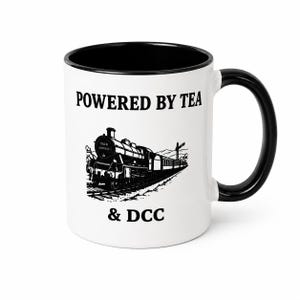K&ouml;nnte beinhalten: Ein wei&szlig;er Keramikbecher mit schwarzem Innenraum und Henkel. Die Vorderseite zeigt eine schwarze Grafik einer Dampflokomotive mit dem Text "POWERED BY TEA" &uuml;ber dem Zug und "& DCC" darunter. Der Zug tr&auml;gt die Aufschrift "TEA & EXPRESS" vorne.